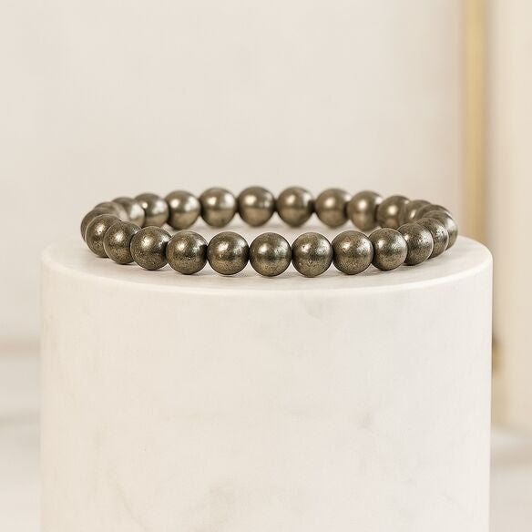 Pyrite beaded bracelet on a white pedestal with a neutral background