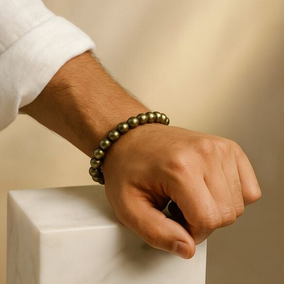 Hand wearing a beaded pyrite crystal bracelet on a neutral background