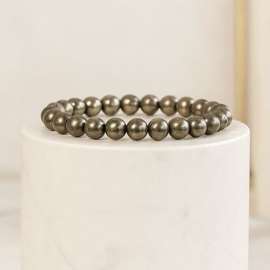 Pyrite beaded bracelet on a white pedestal with a neutral background